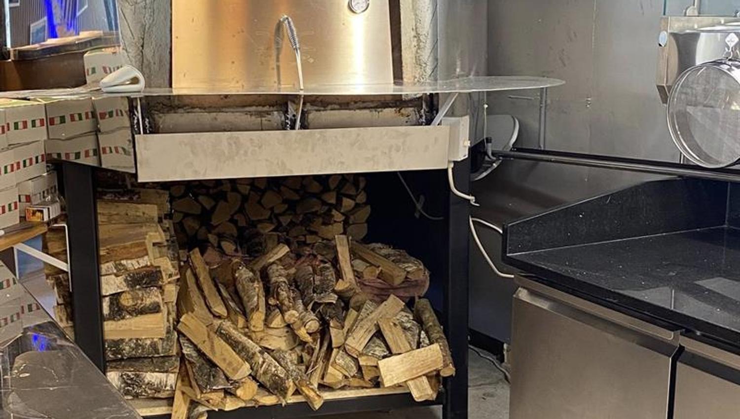Bildet viser en steinovn med en stor vedstabel under for å bake pizza og calzone