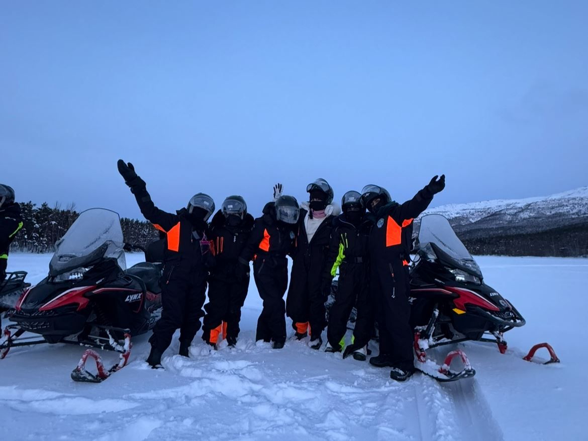 Group gathered between snowmobiles in the Arctic winter landscape