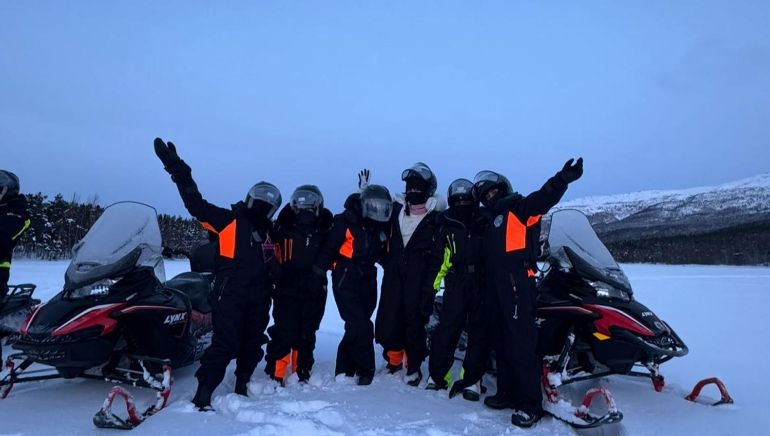 Group gathered between snowmobiles in the Arctic winter landscape