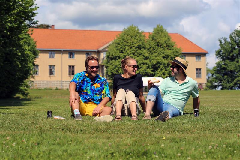 Piknik ved Elingaard – En gruppe mennesker nyter en solrik dag på gresset foran herregården.