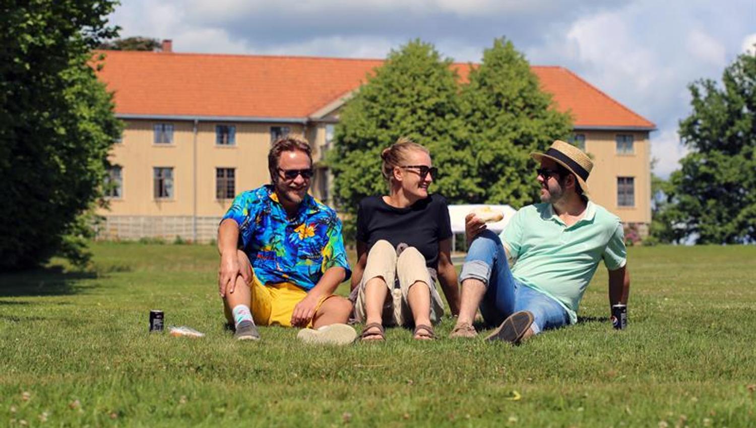 Piknik ved Elingaard – En gruppe mennesker nyter en solrik dag på gresset foran herregården.