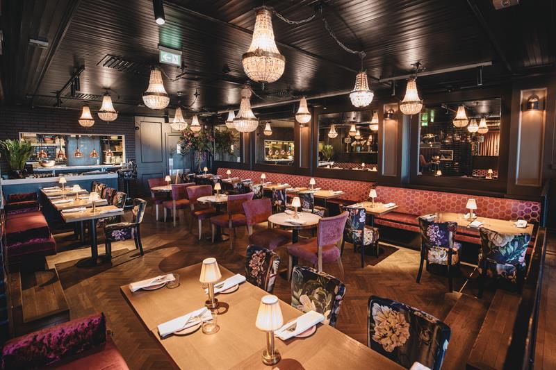 Small tables, chairs and a red seating section. Chandeliers hanging from the ceiling.