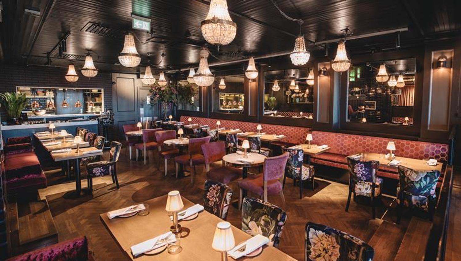Small tables, chairs and a red seating section. Chandeliers hanging from the ceiling.