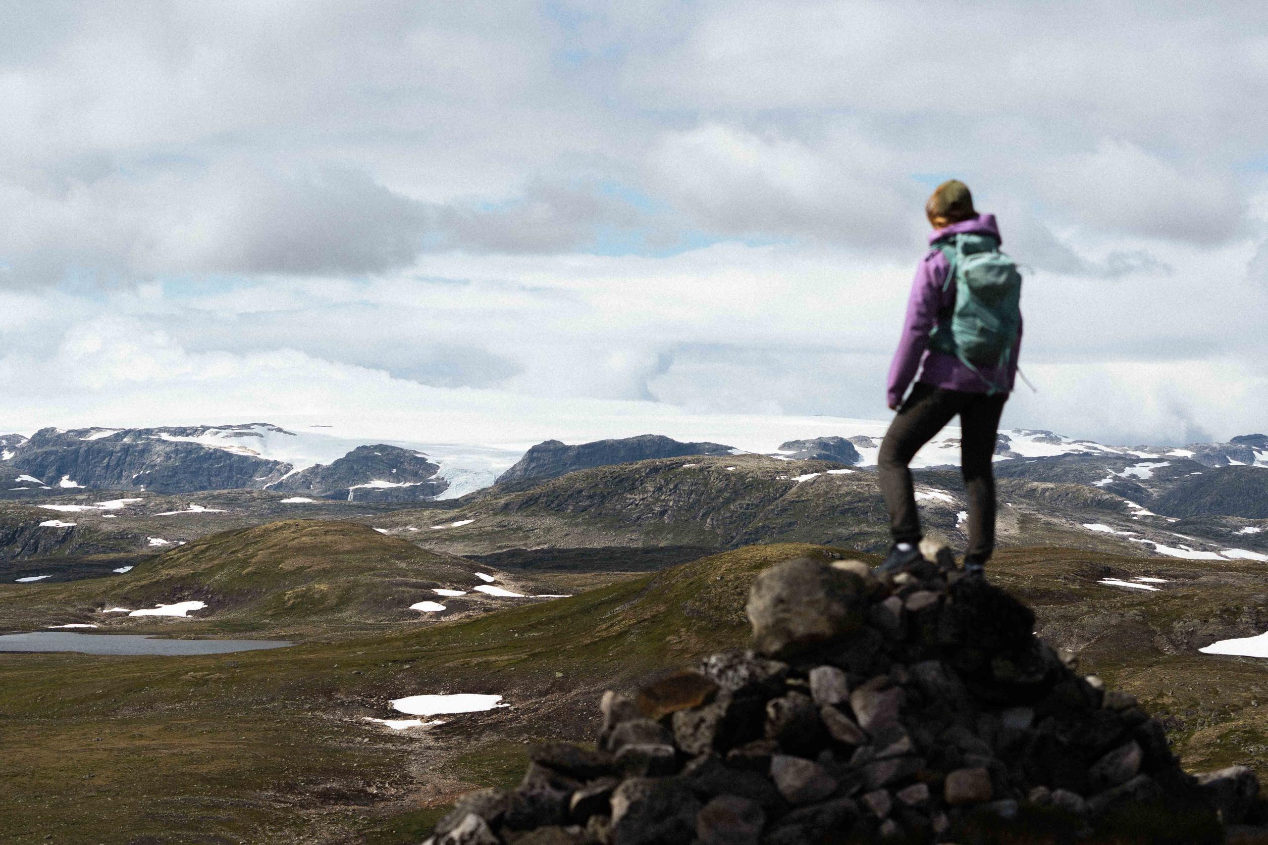 A woman standing on a mountain top gazing towards the Hardangerjøkulen glacier.