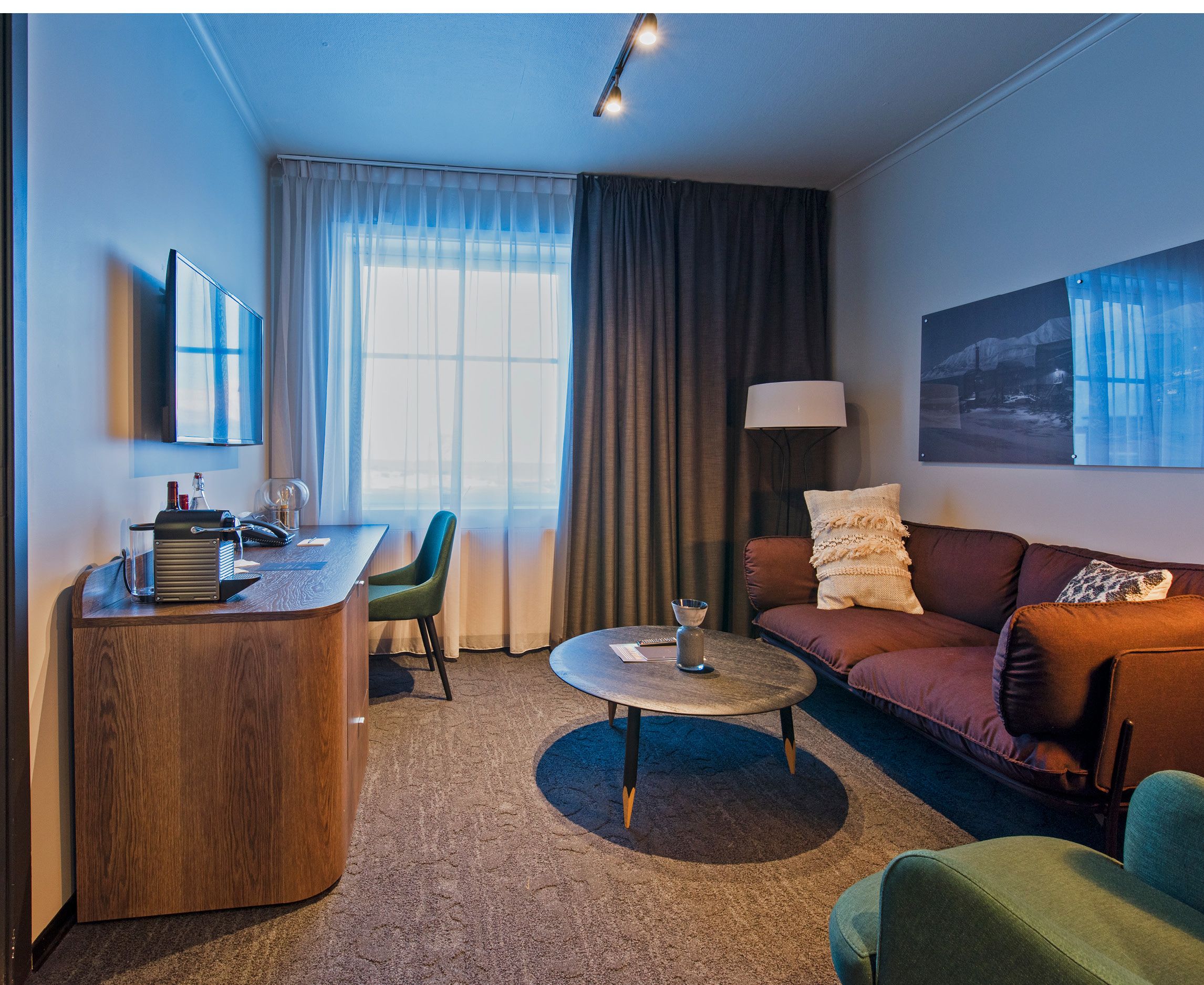A hotel room with a sofa, coffee table and work desk