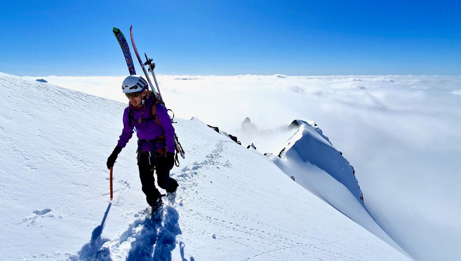 Topptur blant skyer og snøkledde fjell.