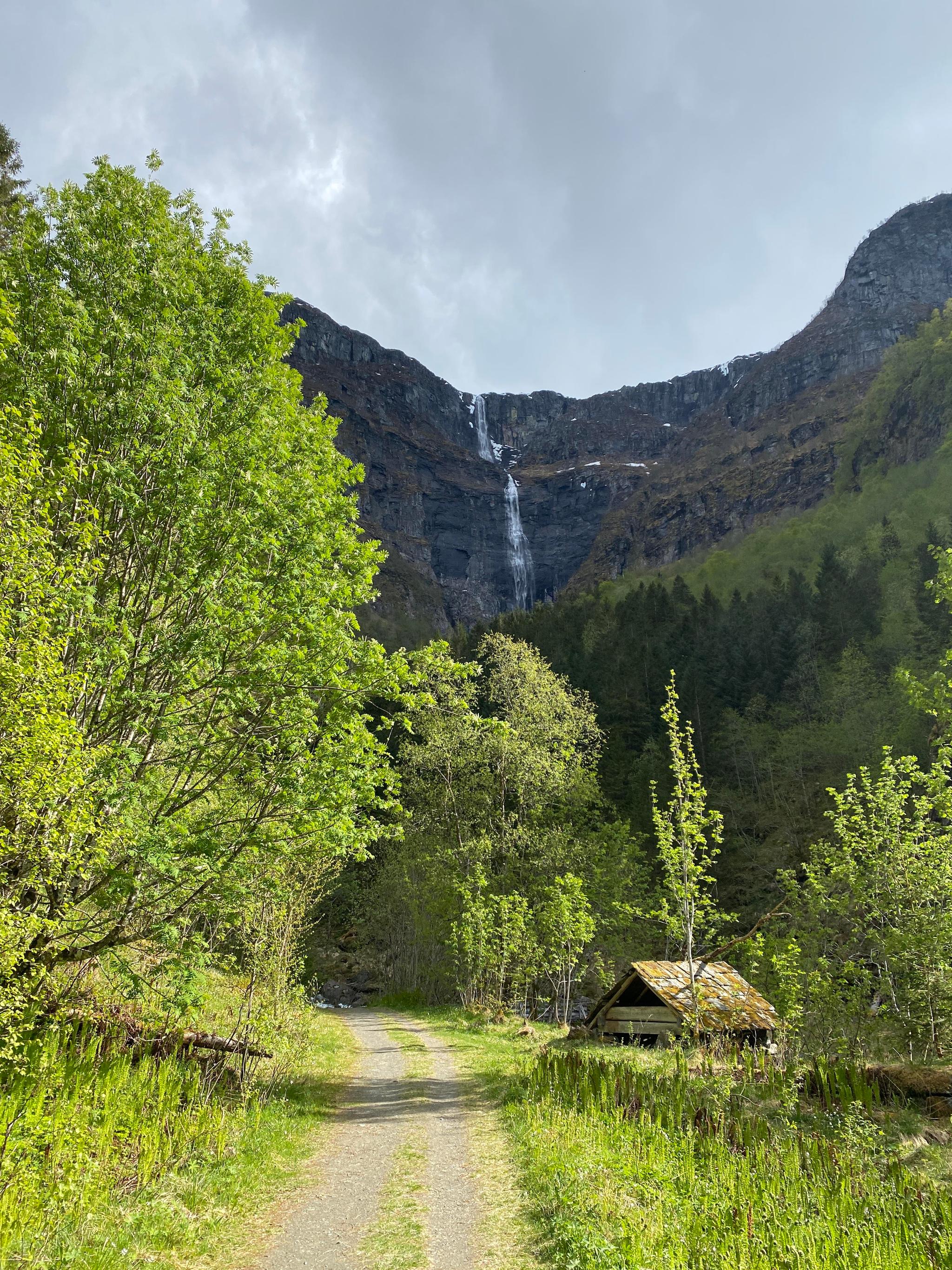 Green valley and gravel road leading towards a tall waterfall in Elvedalen, Lofthus, Hardanger.


