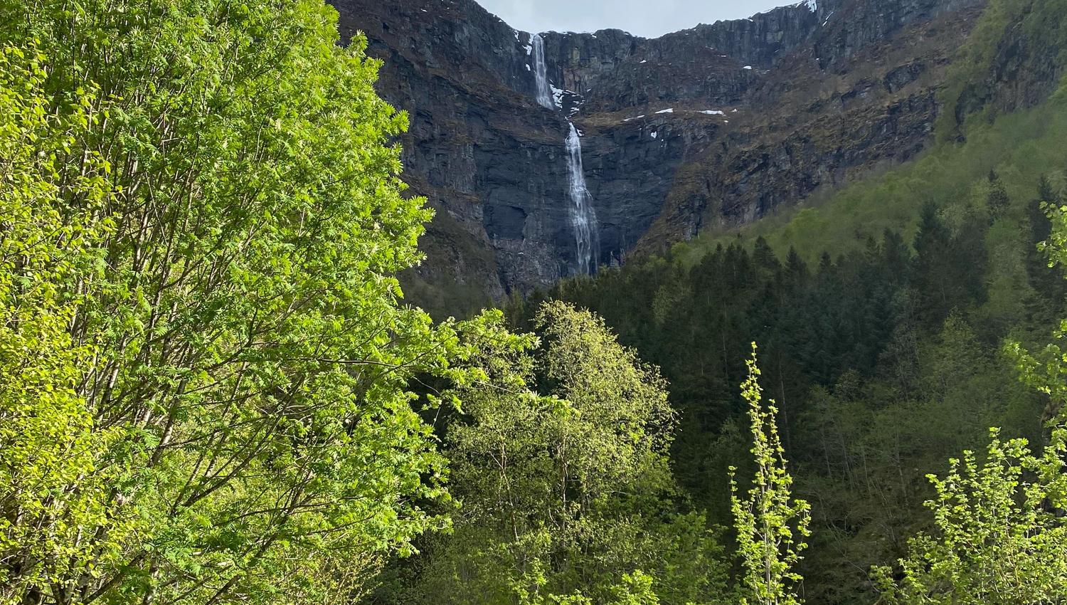 Green valley and gravel road leading towards a tall waterfall in Elvedalen, Lofthus, Hardanger.
