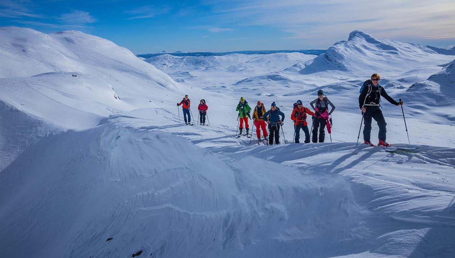 Group of 9 persons on their way up a mountain on randonee skis. Snow covered mountains in the background.