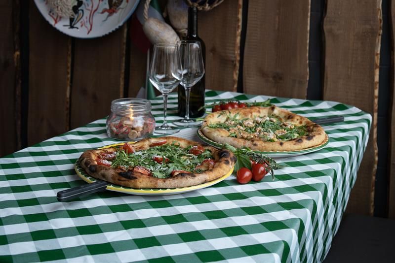 Two pizzas and two wine glasses on a table with a checkered tablecloth