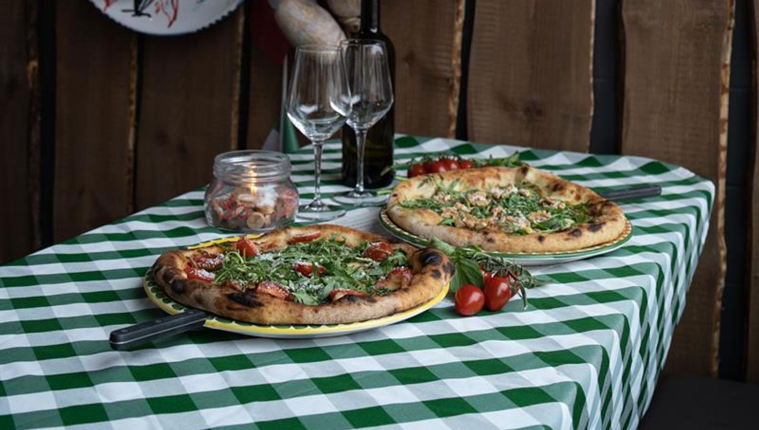 Two pizzas and two wine glasses on a table with a checkered tablecloth