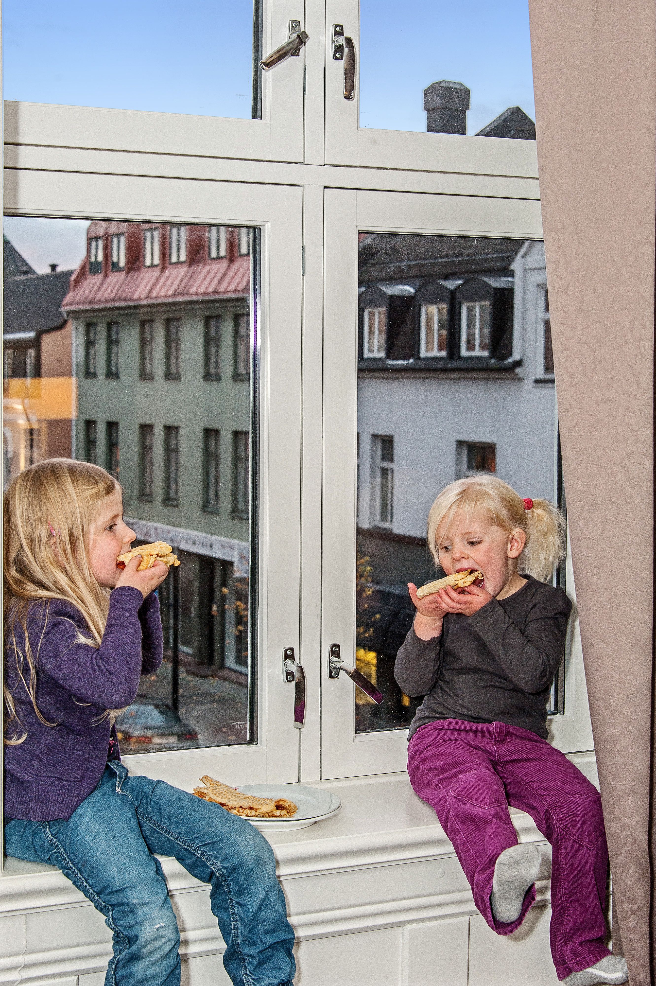 Barn sitter i vinduskarmen og spiser mat