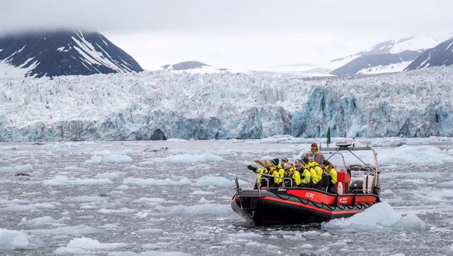 Flere personer i åpen RIB båt foran isbre i isfull fjord