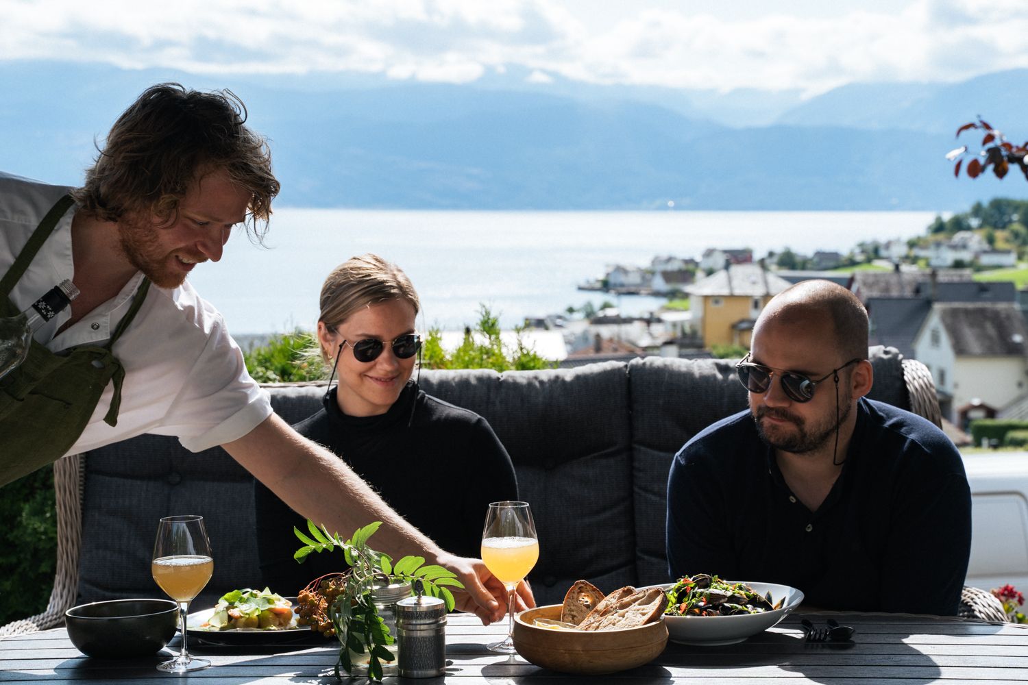 Host serving local food outdoors with fjord view at Eldhuset Farm Restaurant.