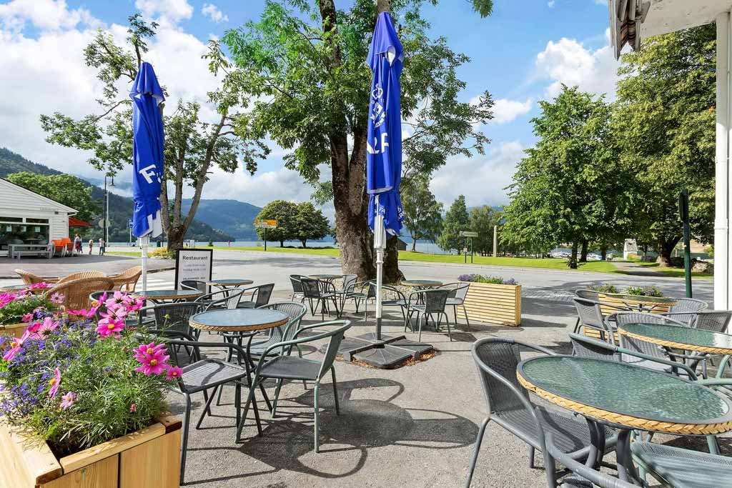 The outdoor area at Kinsarvik Fjordhotel, featuring seating and stunning views of the fjord and mountains.