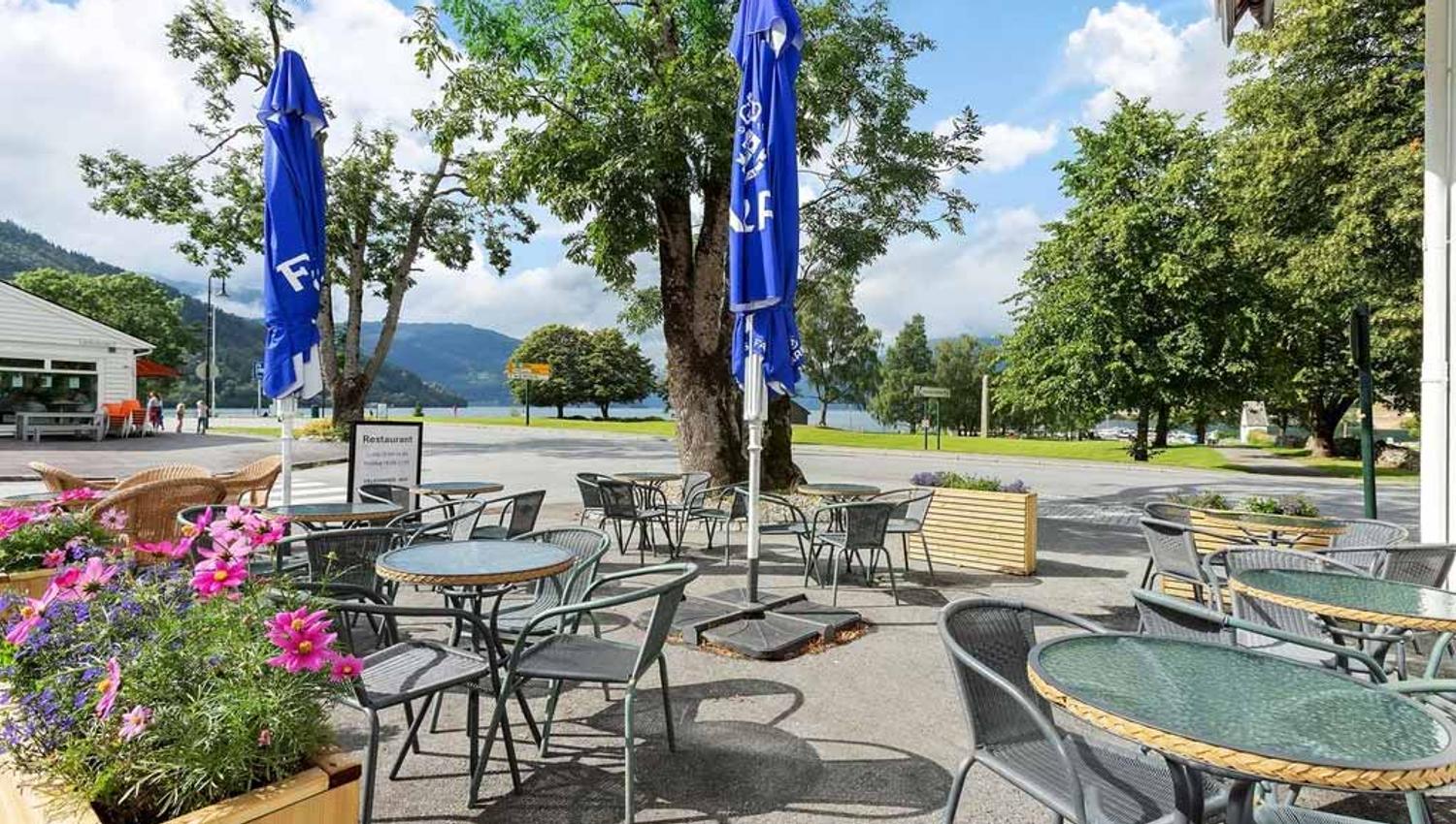 The outdoor area at Kinsarvik Fjordhotel, featuring seating and stunning views of the fjord and mountains.