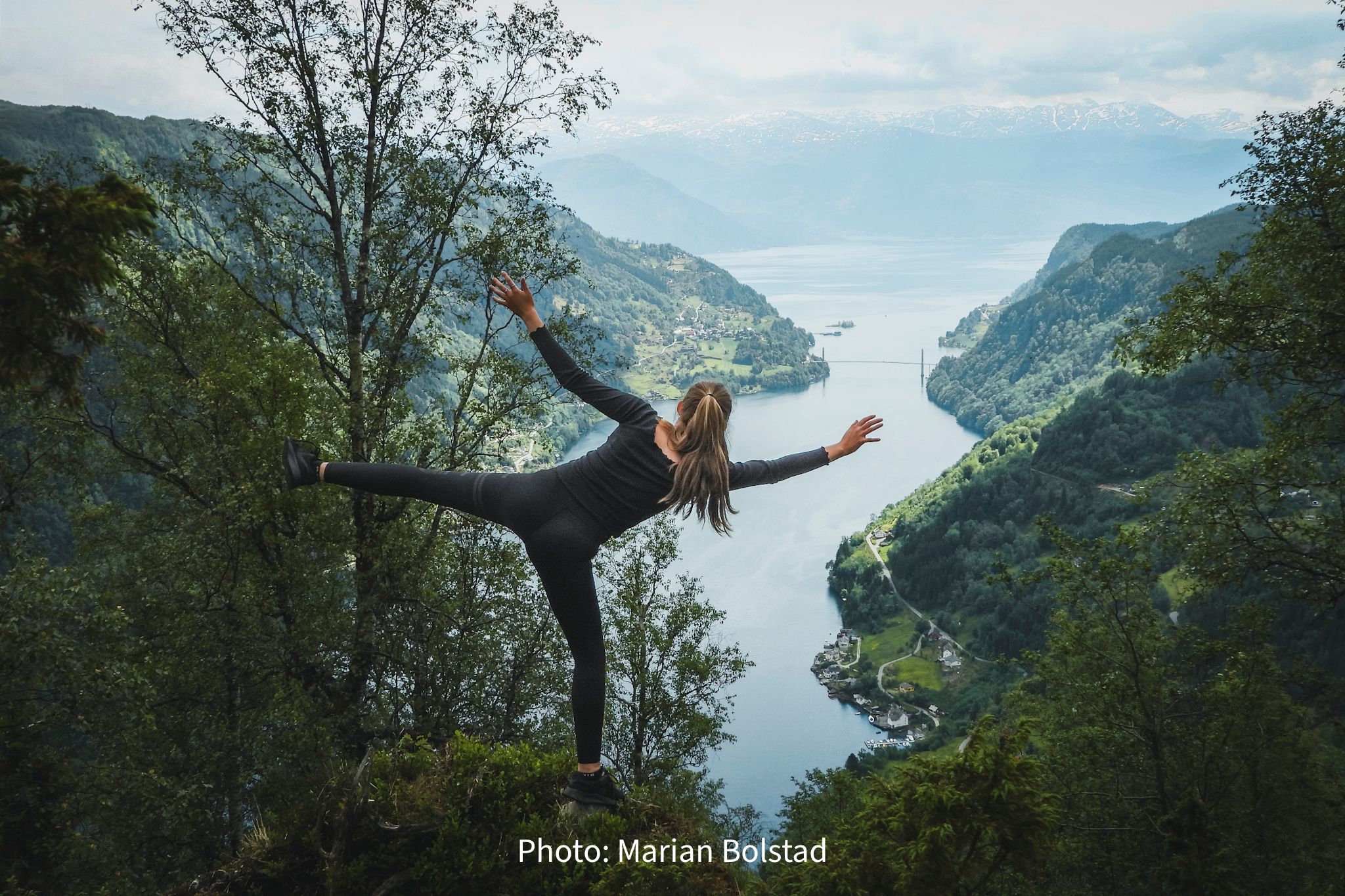Person enjoying a scenic viewpoint overlooking the Hardangerfjord, Norway, with mountains and fjord villages