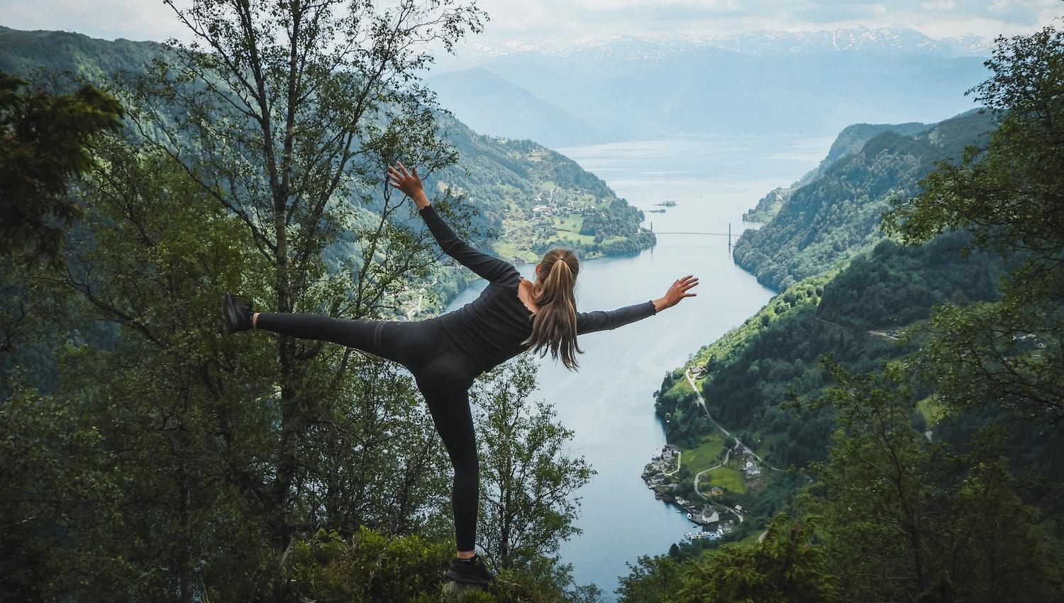 Person enjoying a scenic viewpoint overlooking the Hardangerfjord, Norway, with mountains and fjord villages