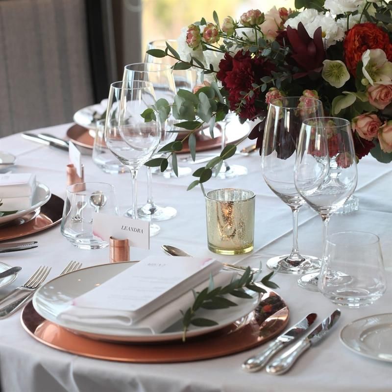 Stilfull borddekking med blomster, vinglass og kobberdetaljer i en lys og elegant spisesal.