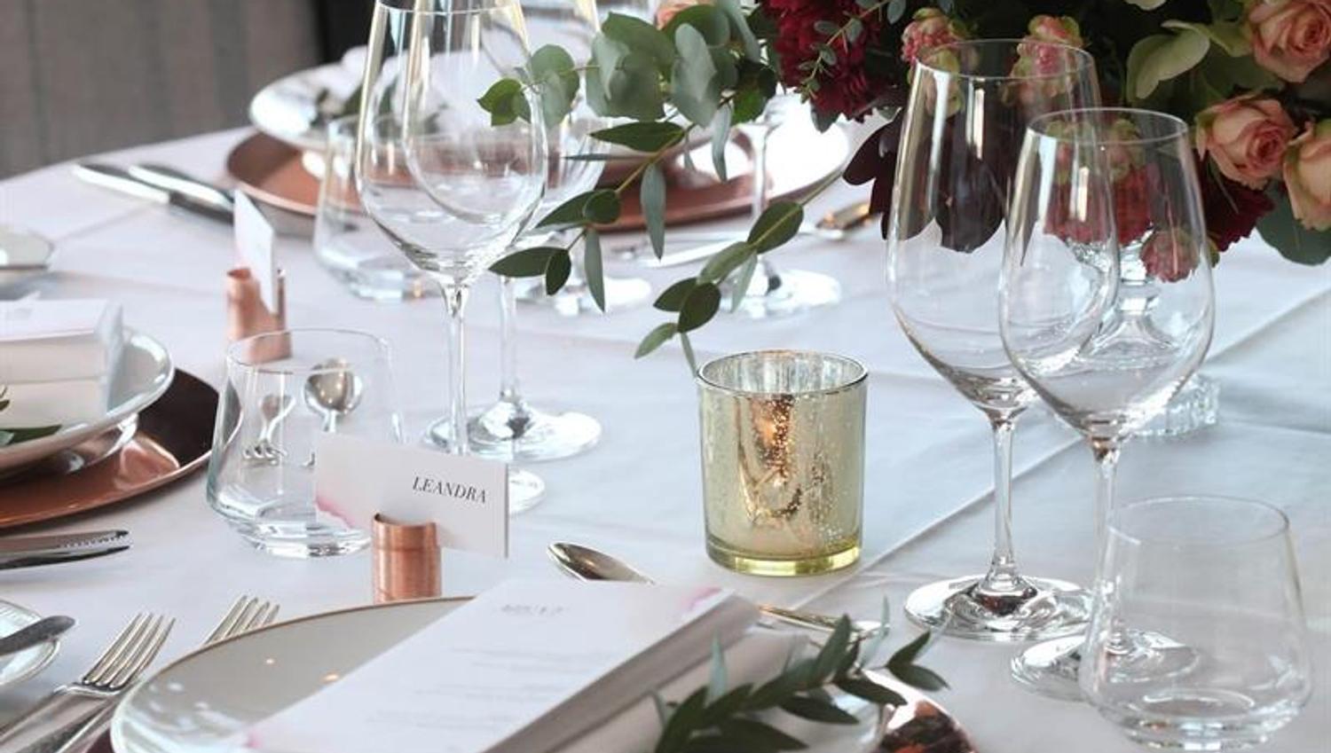 Stilfull borddekking med blomster, vinglass og kobberdetaljer i en lys og elegant spisesal.