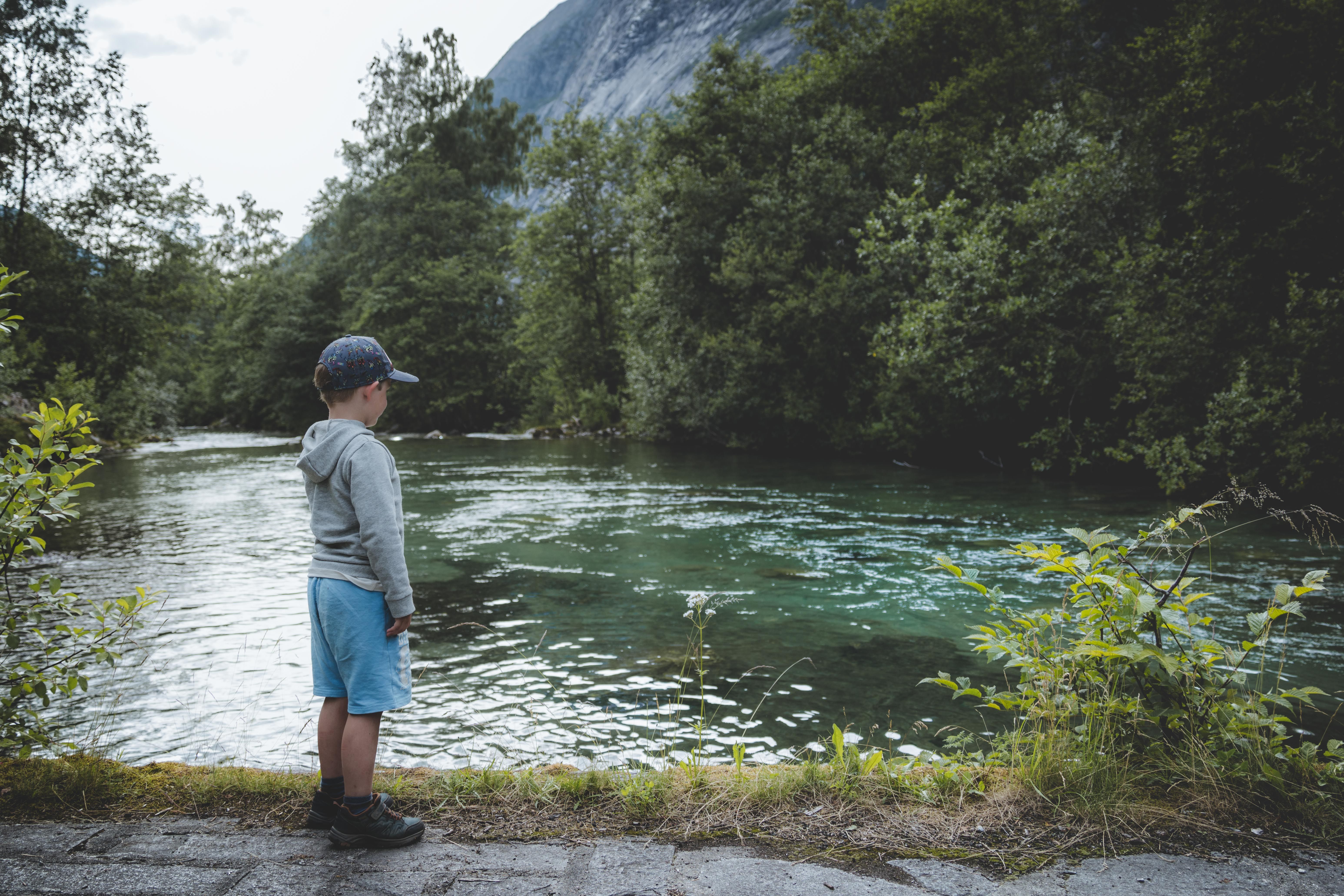 A small boy stands by the turquoise river that flows down the Simadalen valley.