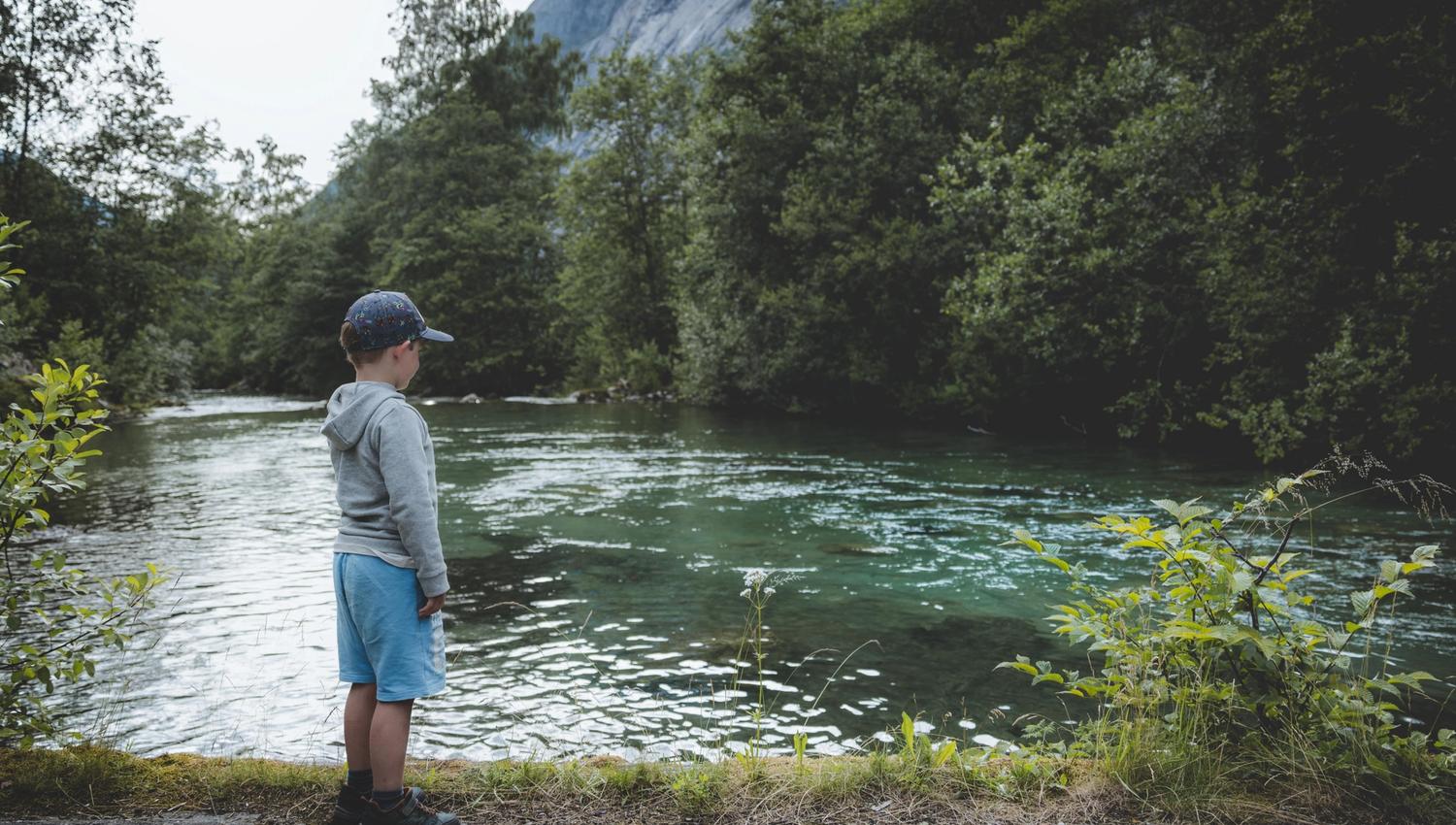 A small boy stands by the turquoise river that flows down the Simadalen valley.