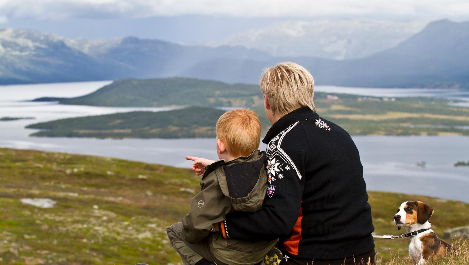adult and child with dog sitting and looking out over the landscape