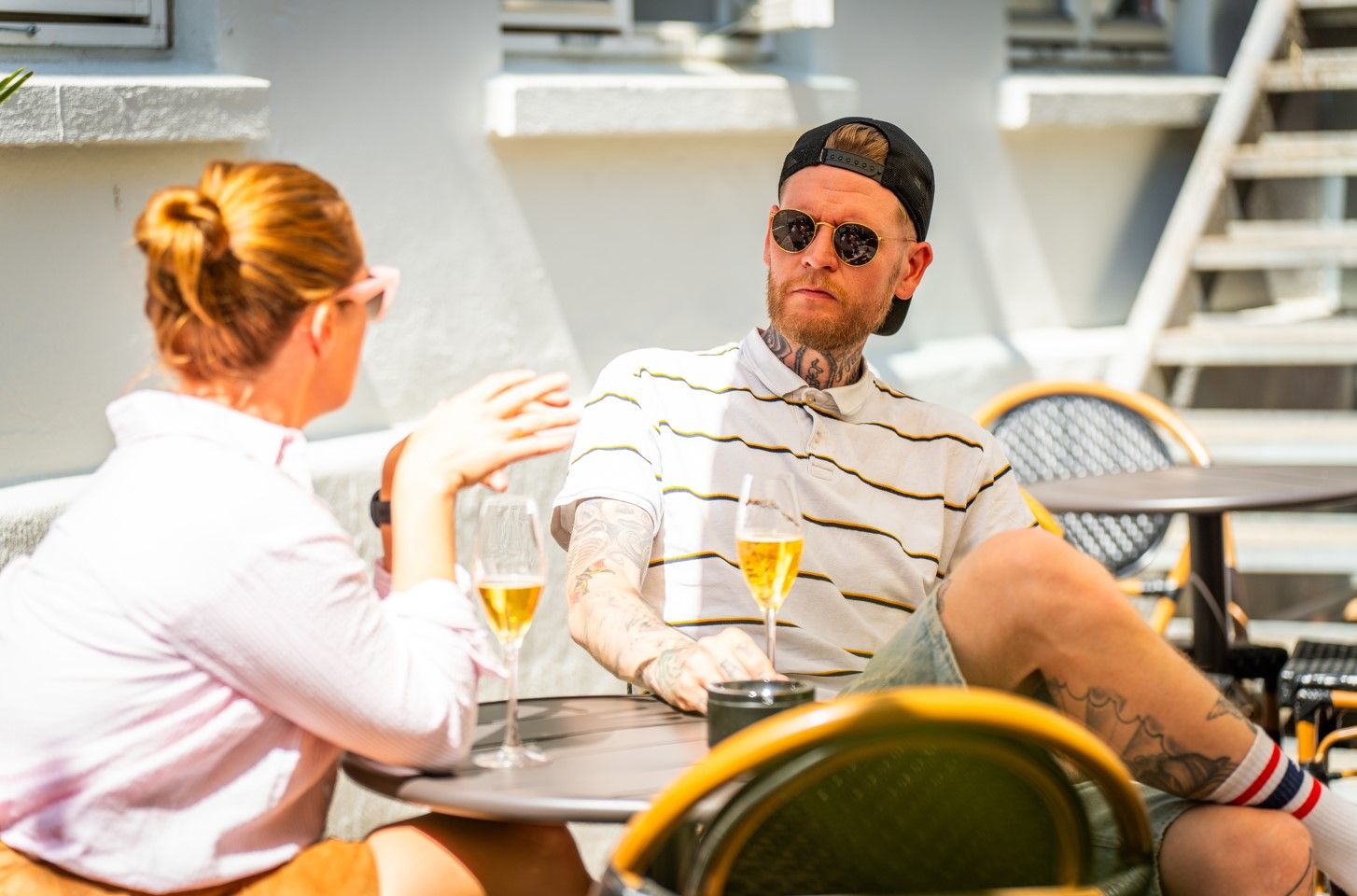 en mann og en kvinne som sitter rundt et bord og snakker mens de drikker vin