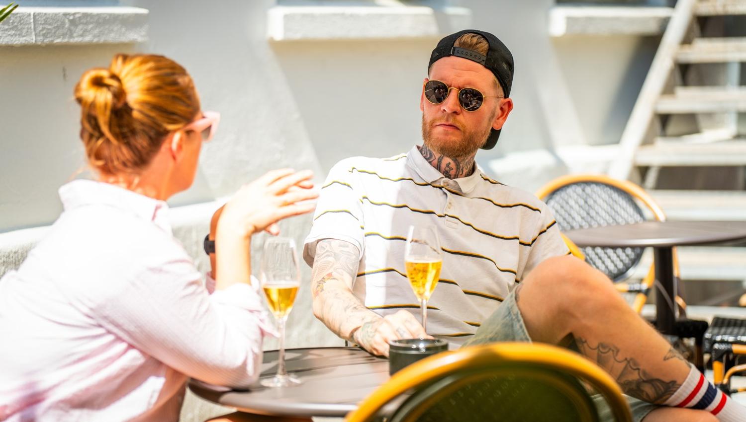 en mann og en kvinne som sitter rundt et bord og snakker mens de drikker vin