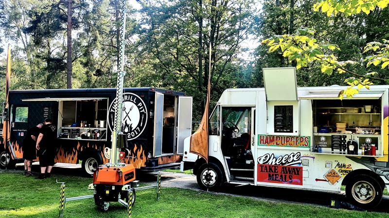 To foodtrucks fra The Grill Pit parkert utendørs ved et skogsområde.