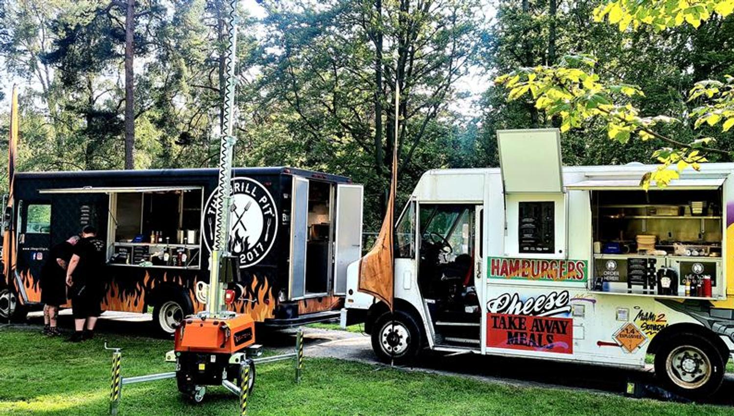 To foodtrucks fra The Grill Pit parkert utendørs ved et skogsområde.