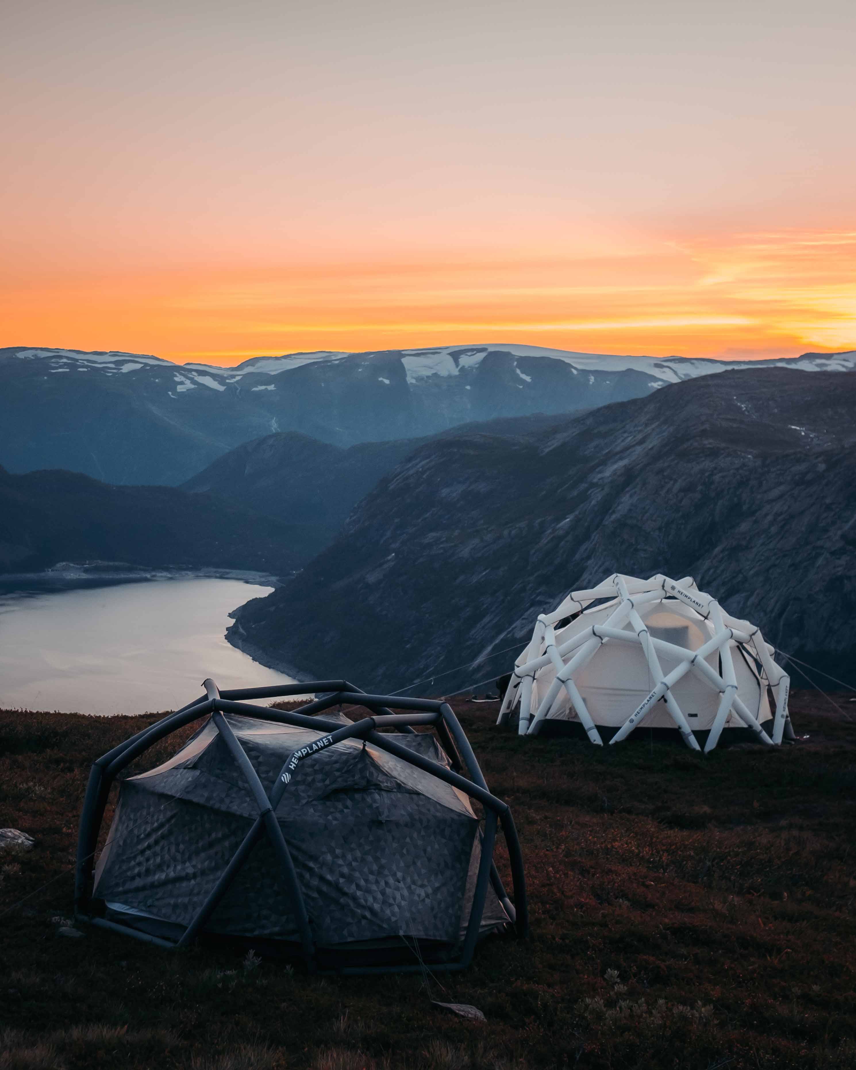 Geodetiske telt på fjelltoppen ved solnedgang med utsikt over en fjord.