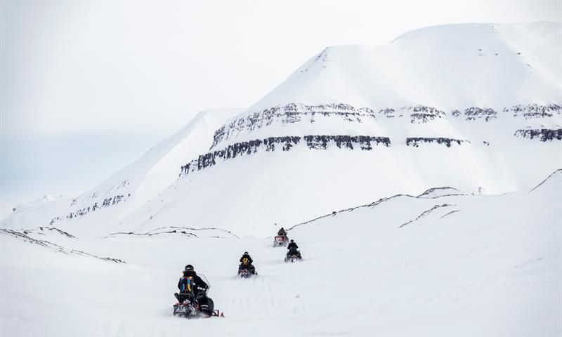 Snøscootere foran snødekte fjell.