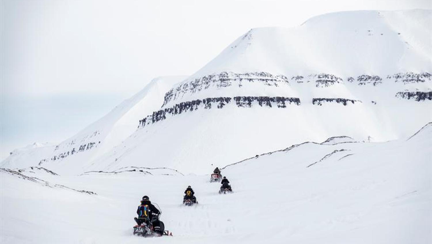 Snøscootere foran snødekte fjell.