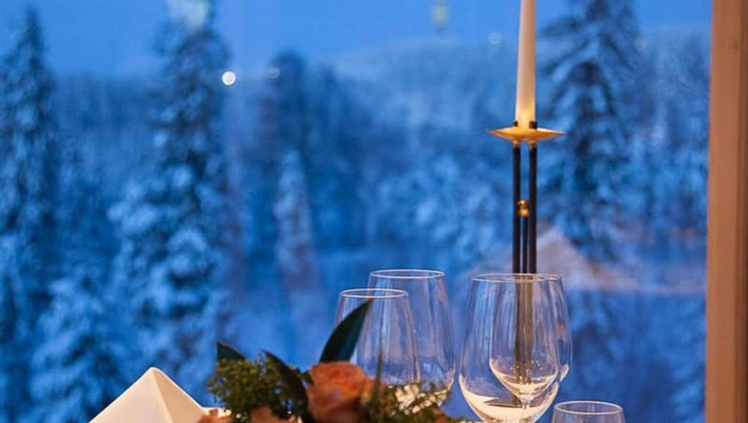 Elegant dekket bord ved vinduet med levende lys og vinterlig skoglandskap utenfor.