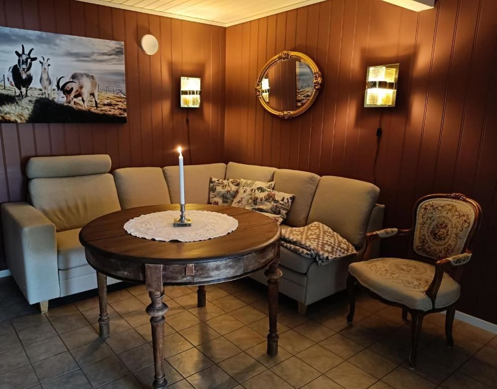 Orheimstunet in Nordfjord - Cozy sitting nook with a sectional sofa, round wooden table with a lit candle, wall lamps, and framed art..