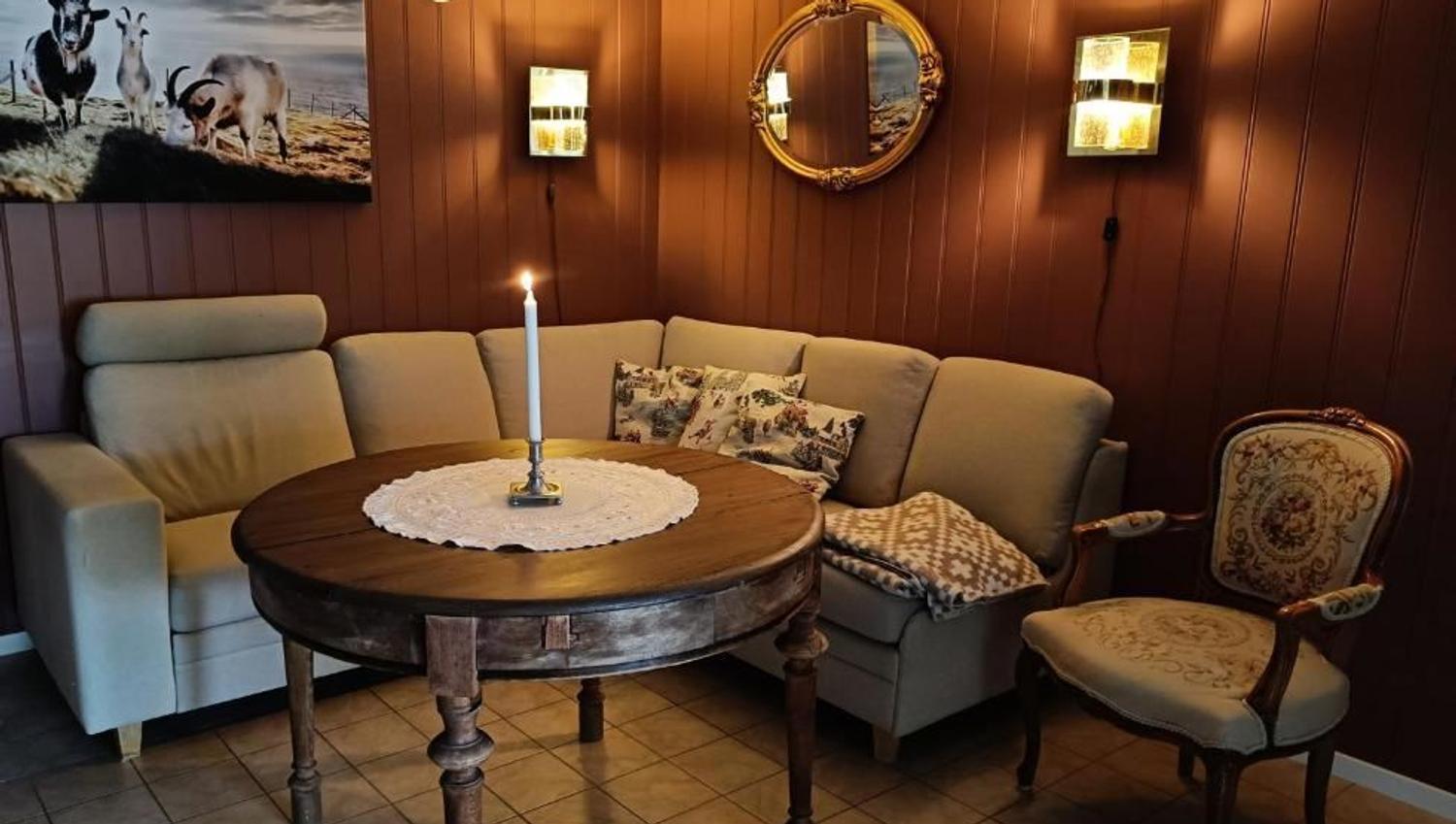 Orheimstunet in Nordfjord - Cozy sitting nook with a sectional sofa, round wooden table with a lit candle, wall lamps, and framed art..