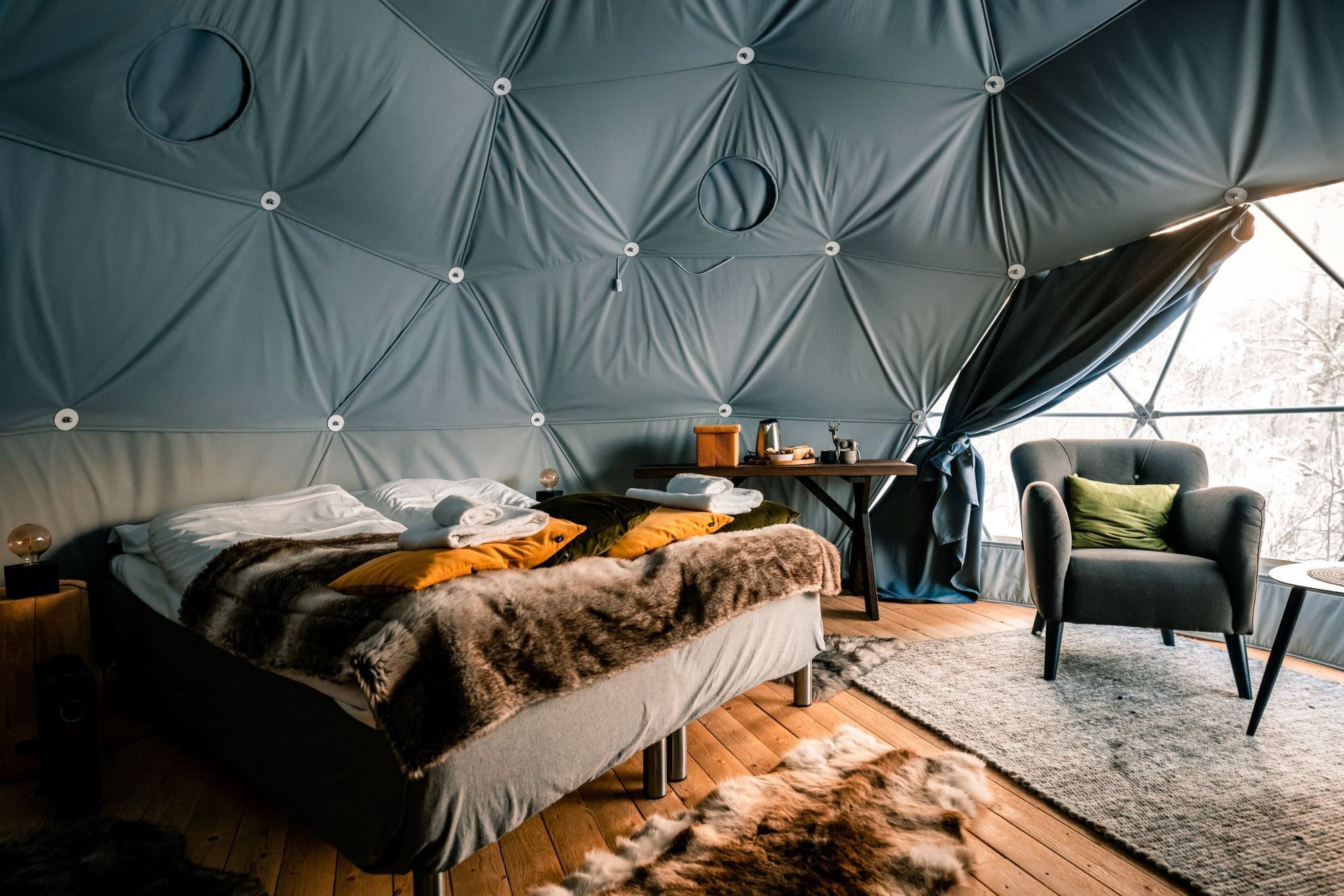 Cozy glamping interior featuring a double bed, armchair, and rustic decor.