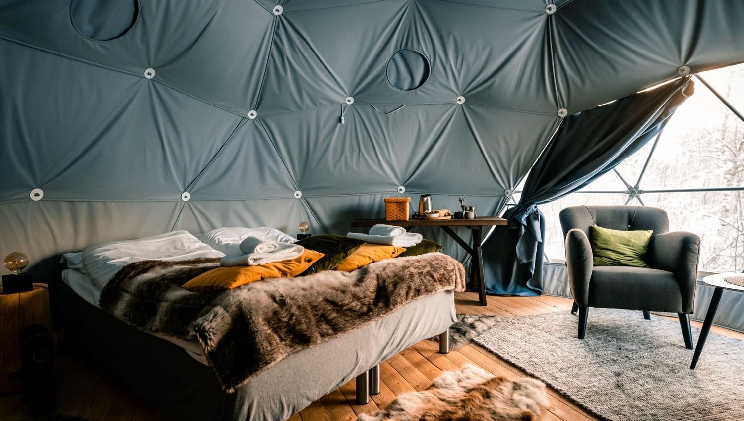 Cozy glamping interior featuring a double bed, armchair, and rustic decor.