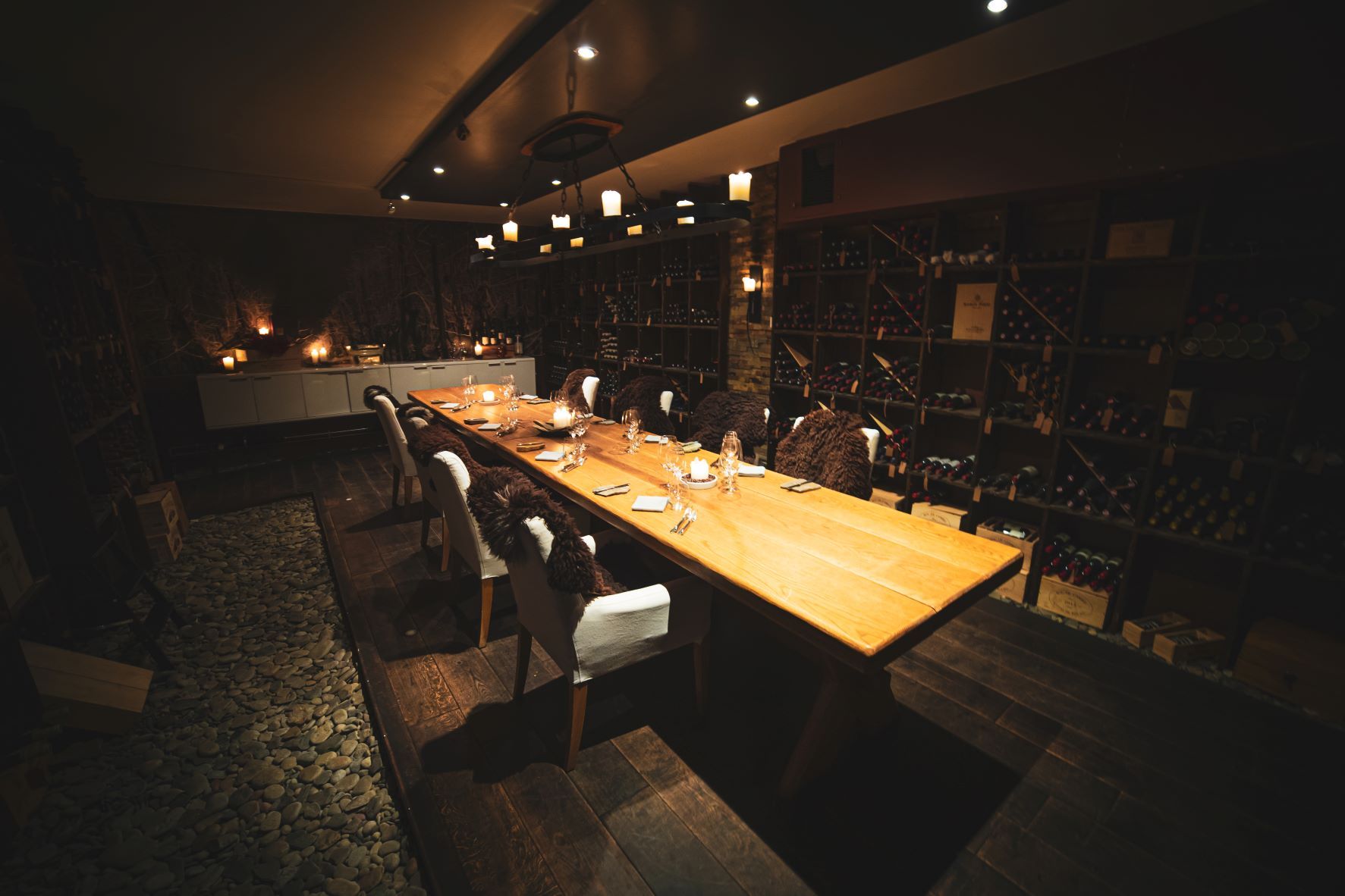 A room with a long table and shelves with wine bottles from floor to ceiling along the wals of the room