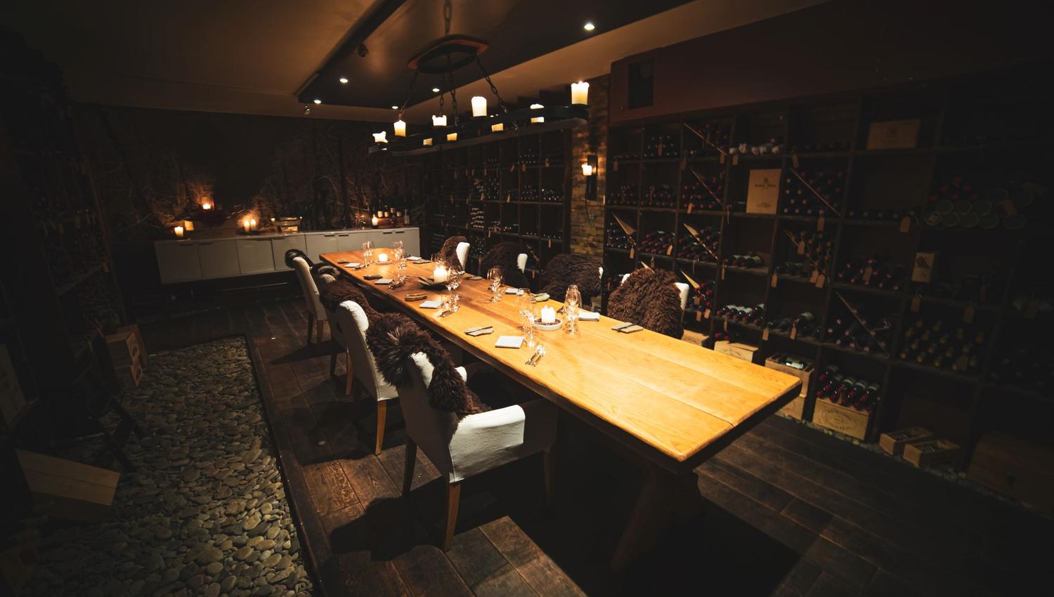 A room with a long table and shelves with wine bottles from floor to ceiling along the wals of the room