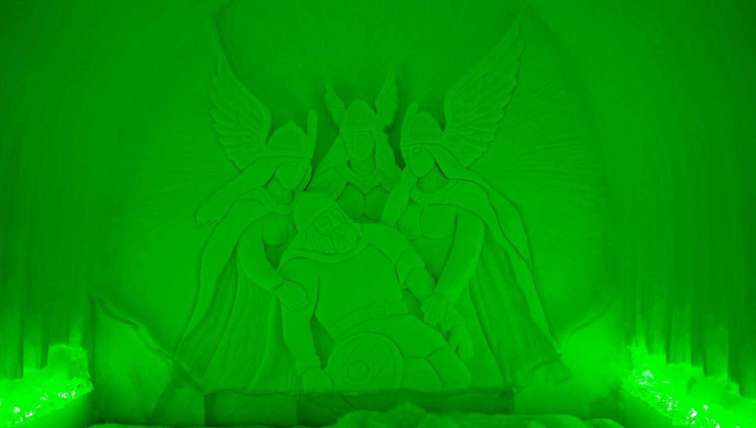Ontdek deze indrukwekkende sneeuwsculptuur, verlicht in een betoverend groen licht. De afbeelding toont mythologische figuren die een held omringen, wat een gevoel van mystiek en avontuur oproept. Een must-see voor elke bezoeker!