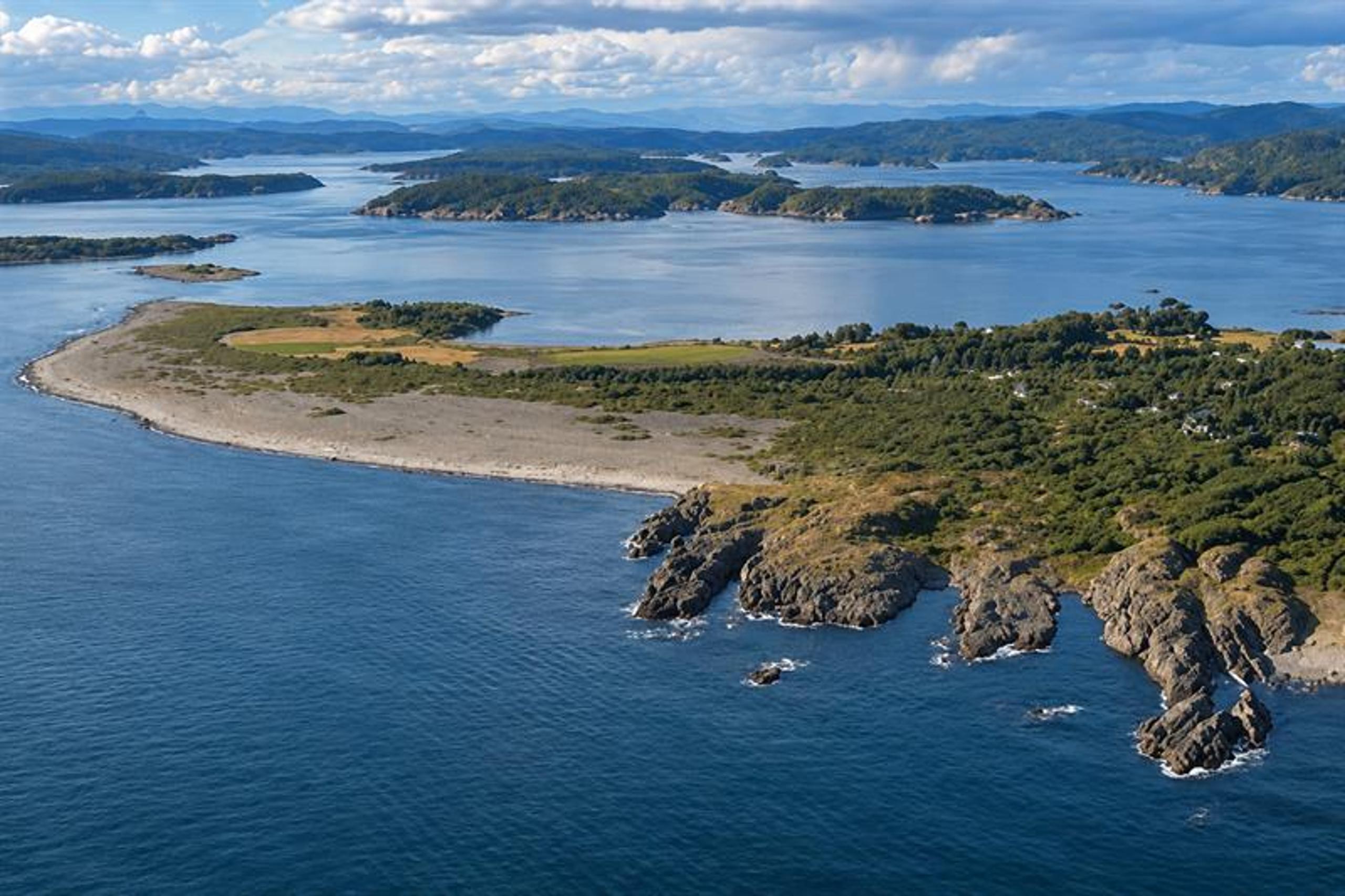 Aerial view of Mølen's curved pebble beach, with islands, islets and coastal waters beyond.