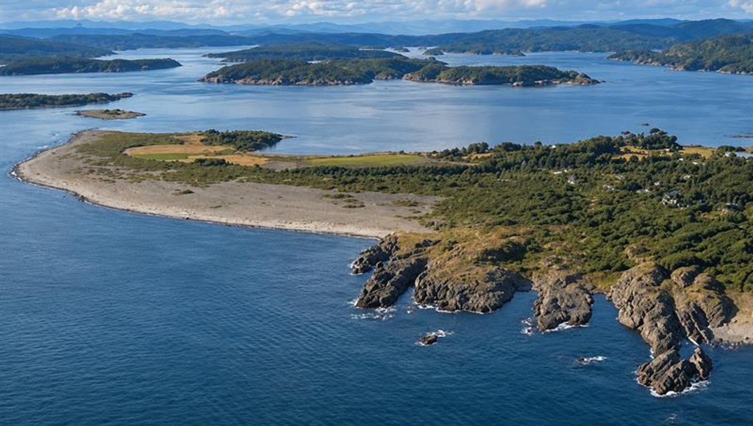 Aerial view of Mølen's curved pebble beach, with islands, islets and coastal waters beyond.