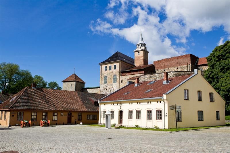 One white and one yellow house with the fortress in the background. Trees on each side.