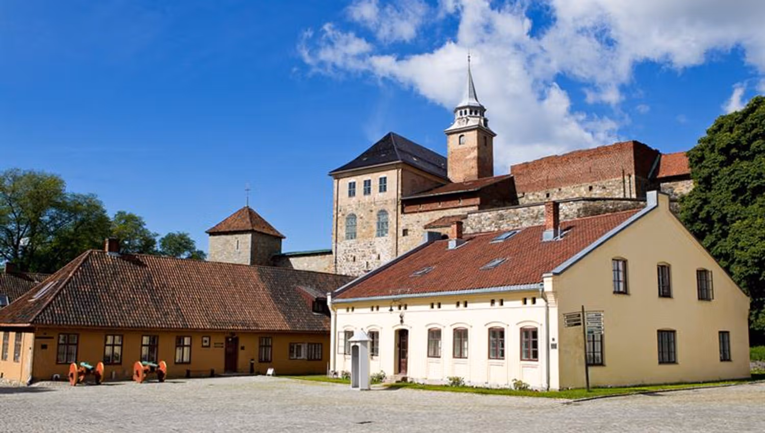 One white and one yellow house with the fortress in the background. Trees on each side.