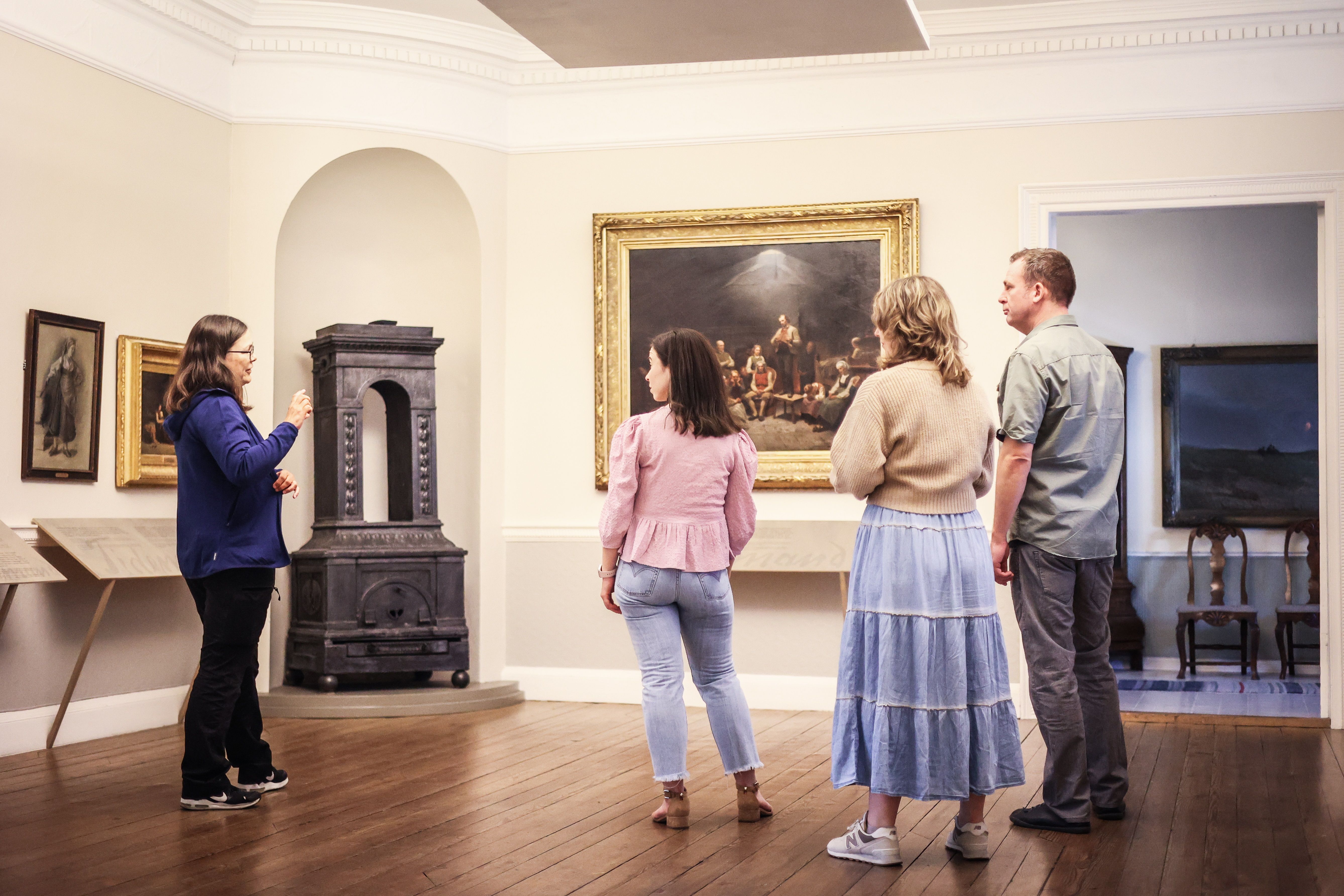 Four people are inside Mandal Museum looking at the large painting “The Haugeans”, where Adolph Tidemand depicts the followers of the lay preacher Han