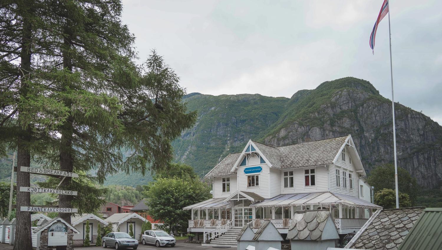 Showing Eidfjord Gjestgiveri from the outside. It's a large wooden house, white, with woodcarved details.