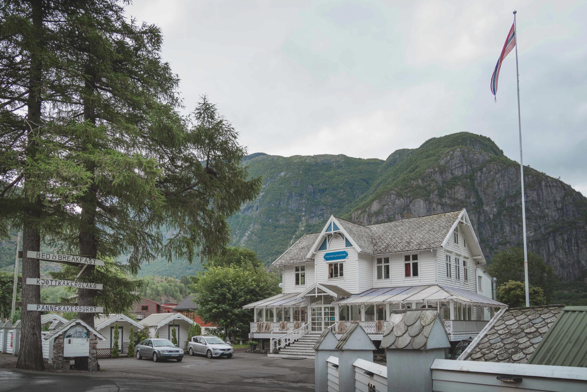 Showing Eidfjord Gjestgiveri from the outside. It's a large wooden house, white, with woodcarved details.