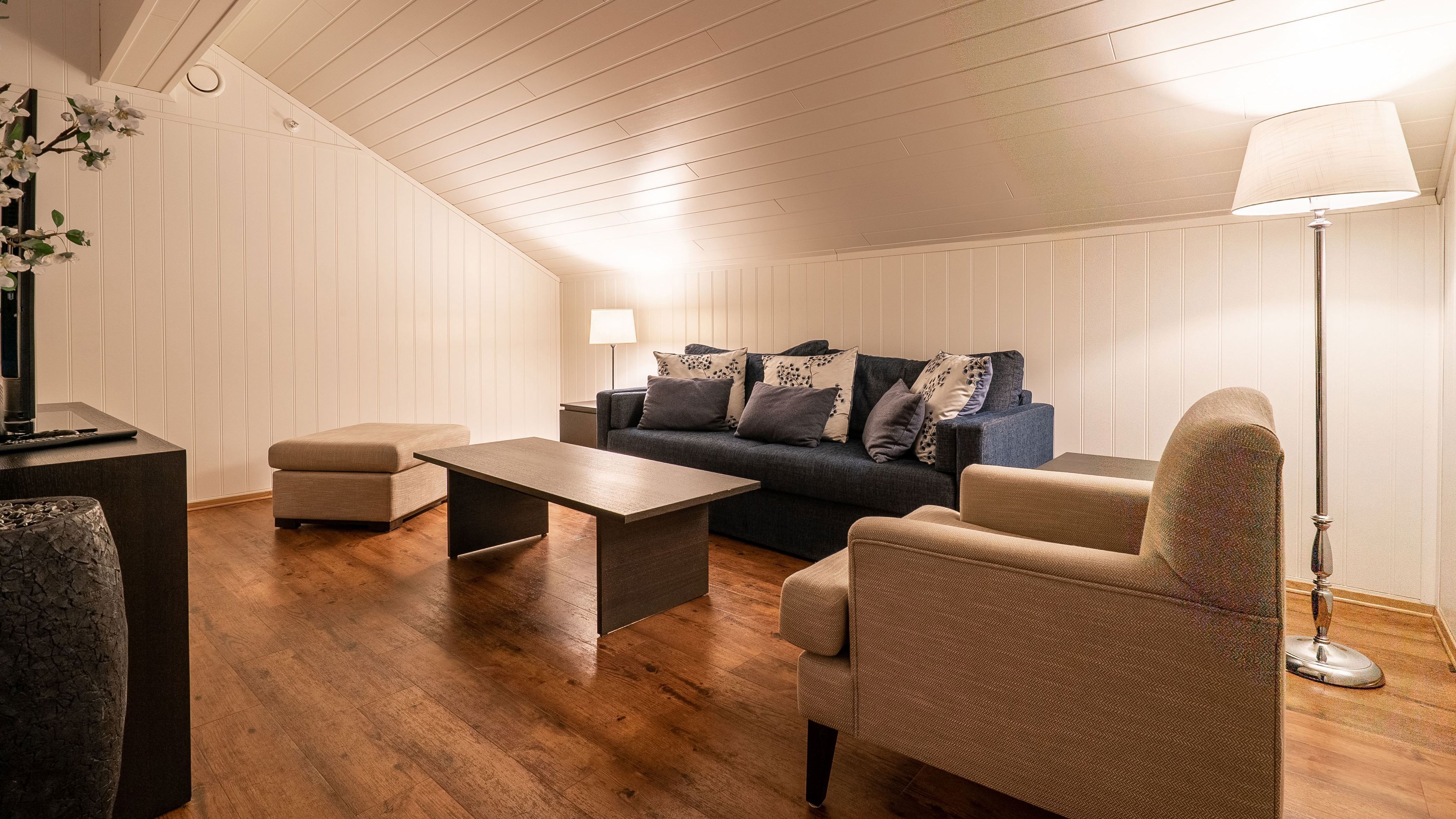 Living room with slanted ceiling, blue sofa, beige armchairs, and wooden floor